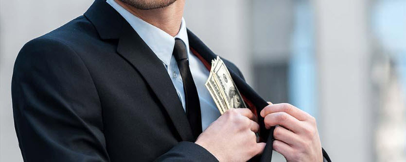 Man in suit putting 100 dollar bills in his pocket